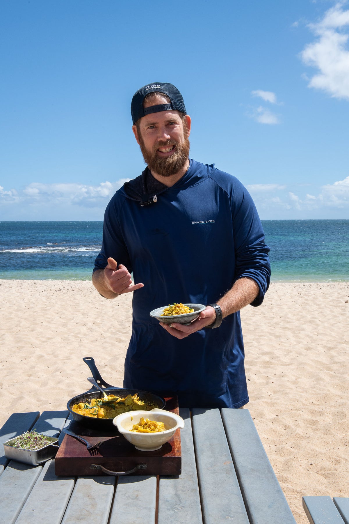 Chef Glen in a Shark Eyes hoodie presenting a dish on the beach